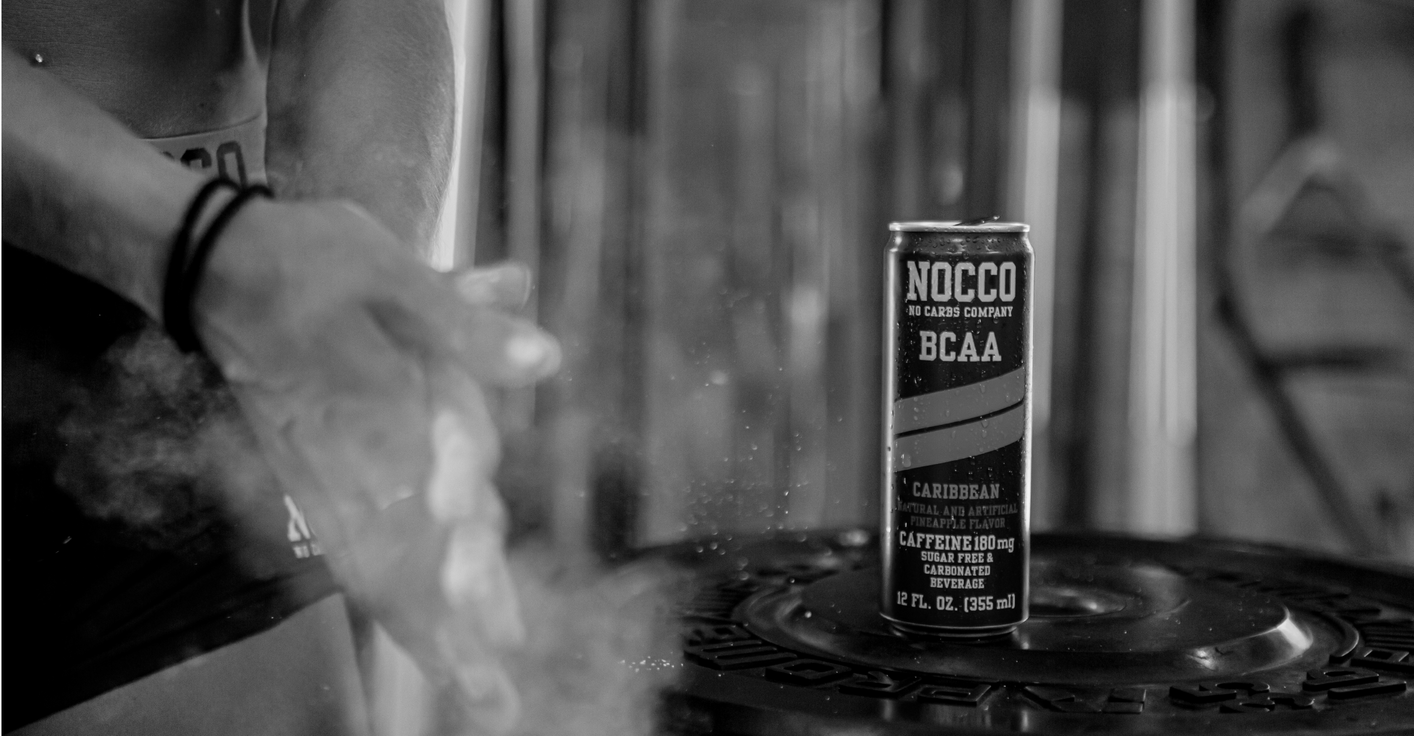 Black and white photo of a person's arm and a NOCCO BCAA drink can on a weight plate.