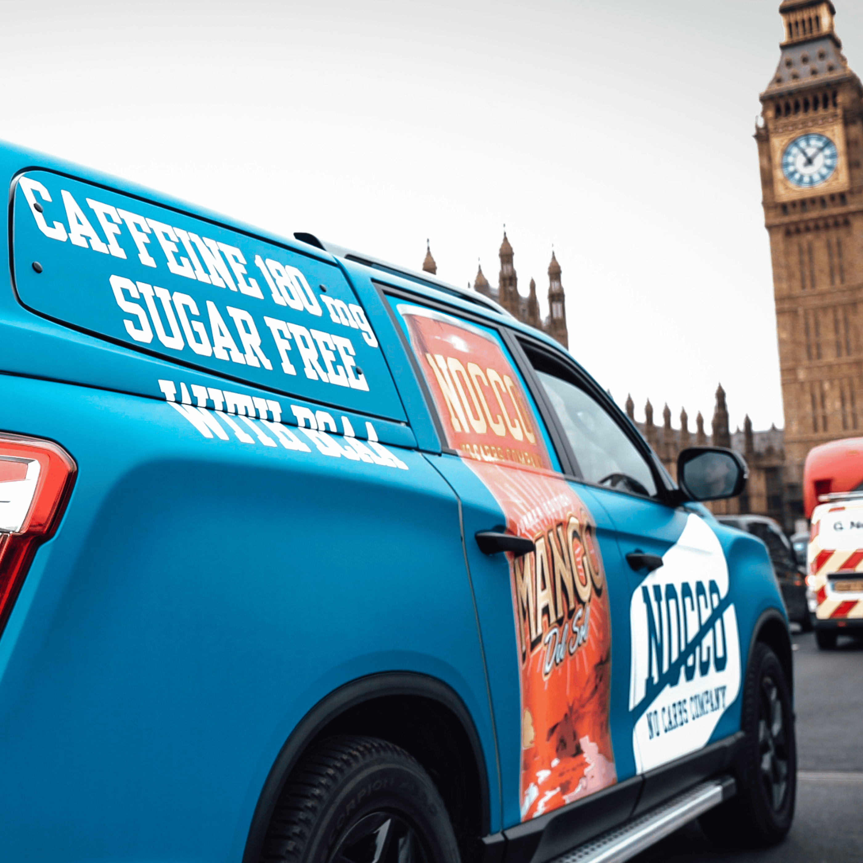 Blue promotional vehicle with ads for a caffeine drink near Big Ben in London.
