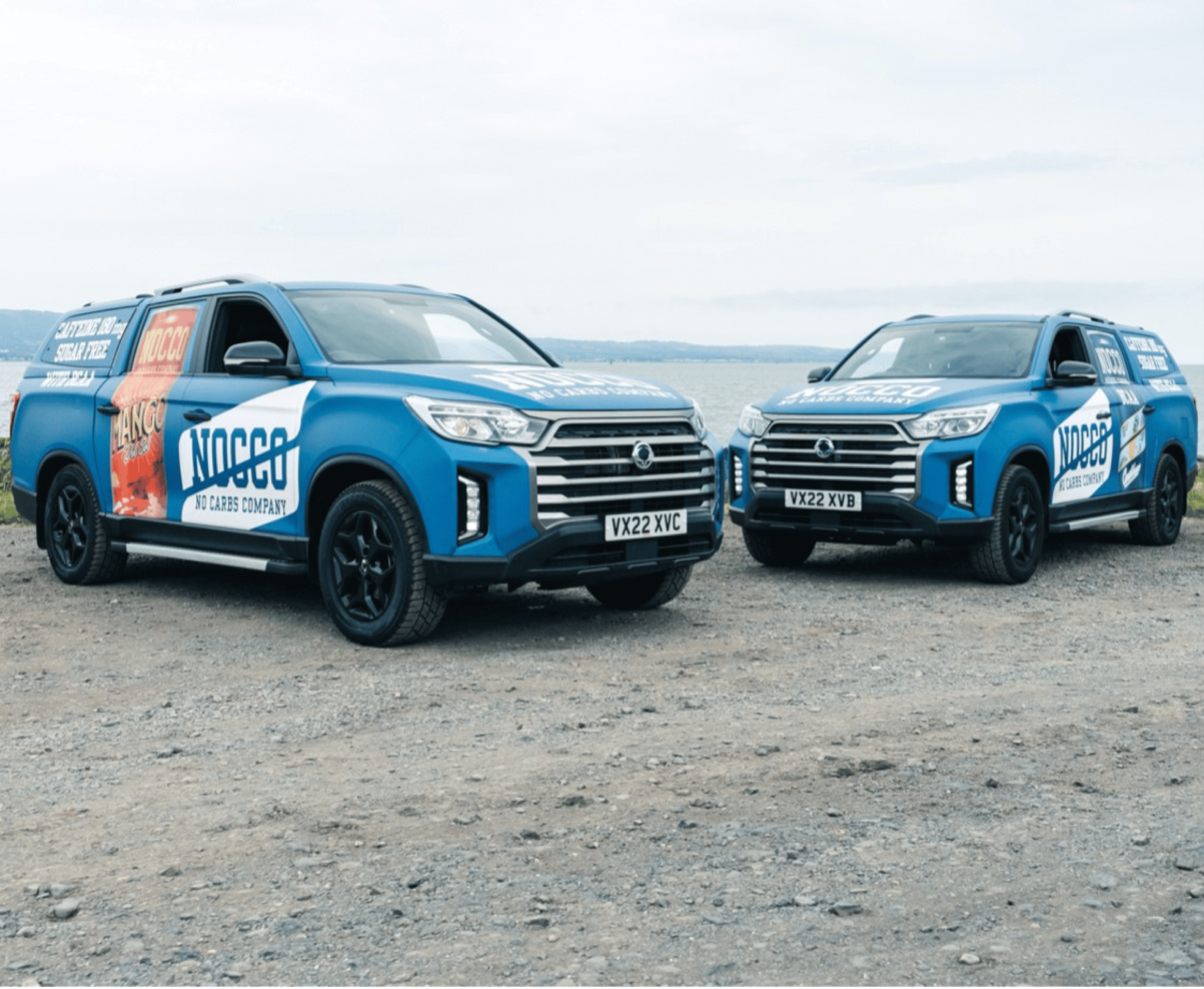 Two blue pickup trucks with promotional decals parked near a lake.