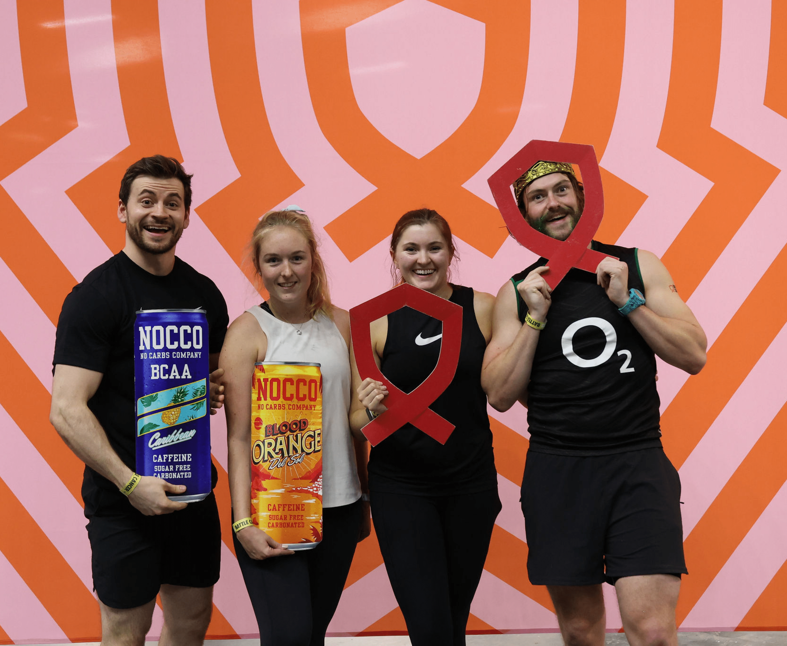 Four people posing with props, against an orange zigzag backdrop.